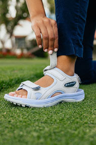 woman fastening the top adjustable Velcro strap on an Orlimar Ladies Golf Sandal