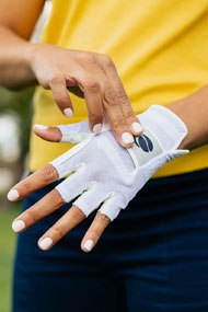 woman with a yellow shirt fastening the Velcro closure with her right hand on an Orlimar Allante half finger golf glove