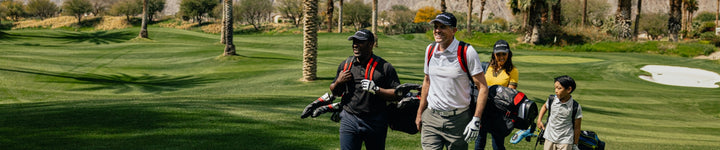 a foursome of golfers of different races and ages carrying golf bags up the fairway