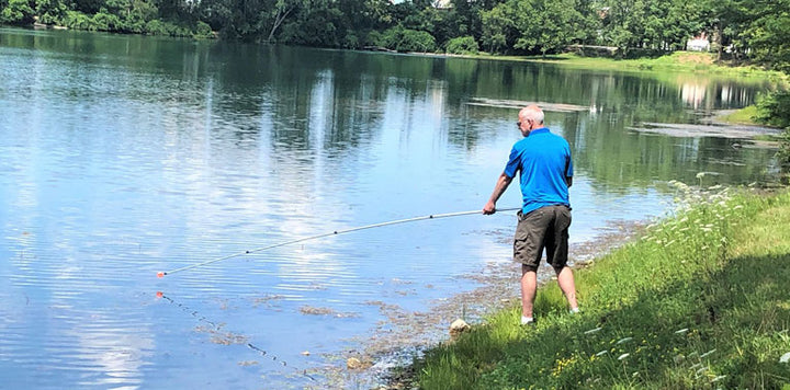 man with shorts and blue golf polo shirt using a Orlimar Fluorescent Head Golf Ball Retriever to retrieve a golf ball from a lake