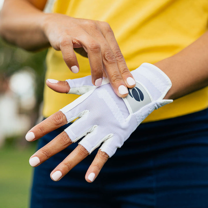 womena putting a white Orlimar half finger golf glove on her left hand