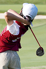 follow through of a junior golfer with a red and white shirt and white hat with an Orlimar logo hitting an Orlimar junior driver with a red shaft