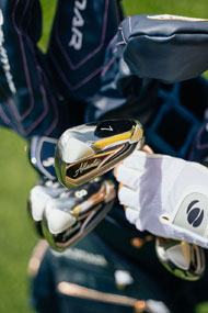 a person wearing a white Orlimar golf glove pulling a 7 iron from a golf bag