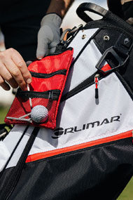 person putting a tee in the mesh pocket of a red Orlimar Golf Detachable Accessory Pouch attached to an Orlimar golf bag