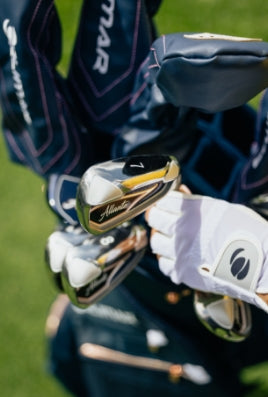a person with a white Orlimar golf glove pulling a 7 iron from a golf bag