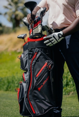 man whearing a white golf glove pulling a club from a black and red Orlimar golf bag out on a golf course