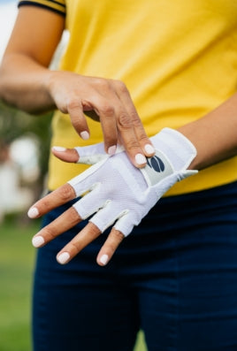 woman with a yellow shirt fastening the Velcro closure with her right hand on an Orlimar Allante half finger golf glove