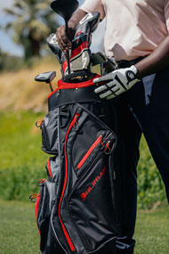 man whearing a white golf glove pulling a club from a black and red Orlimar golf bag out on a golf course