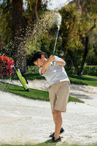 young kid hitting an Orlimar junior golf club from out of a bunker with lime green golf bag in the background