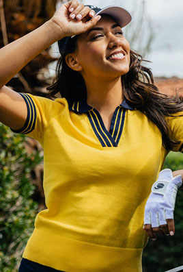 smilaing woman with a yellow shirt, holding the bill of an Orlimar hat, wearing an Orlimar golf glove on her left hand